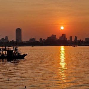 Un viaggio di gruppo WeRoad su un battello a due piani naviga sull'acqua al tramonto, con lo skyline di una città in silhouette sullo sfondo.