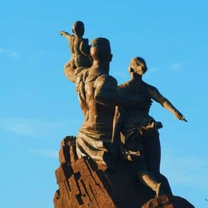 Un gran monumento de bronce de una familia, un hombre, una mujer y un niño, de pie sobre un pedestal rocoso contra un cielo azul claro.