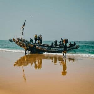 Un grupo de personas se reúne en y alrededor de una barca de madera tradicional en una playa de arena mojada junto al mar.