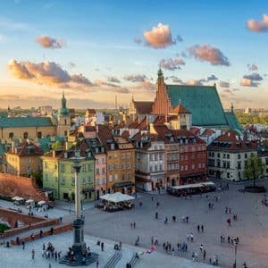 Eine Luftaufnahme eines belebten historischen europäischen Stadtplatzes mit farbenfrohen Gebäuden und einem Glockenturm bei Sonnenuntergang.