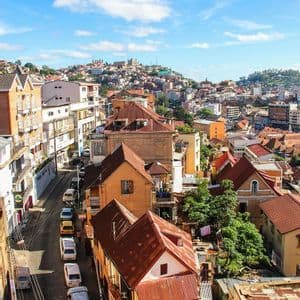 A high-angle view of a dense city on a hill, with colorful buildings, red tile roofs, and a narrow street below.