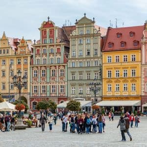 Eine WeRoad Gruppenreise steht auf einem großen Kopfsteinpflasterplatz vor einer Reihe farbenfroher, historischer Gebäude im europäischen Stil.