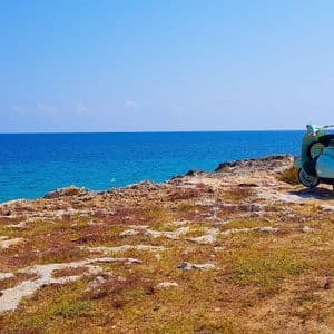Uno scooter d'epoca azzurro parcheggiato su una scogliera rocciosa a picco sull'oceano blu sotto un cielo sereno.