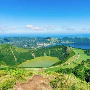 A panoramic view of two volcanic crater lakes, one green and one blue, nestled among lush hills with the ocean in the distance.