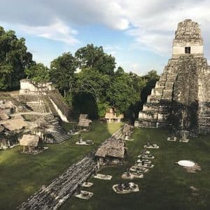 La luce del sole illumina un'antica piramide di pietra e rovine in un'ampia radura erbosa all'interno di una fitta giungla.