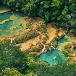 Una vista aerea di piscine terrazzate di acqua turchese e cascate circondate da una foresta lussureggiante e verde.