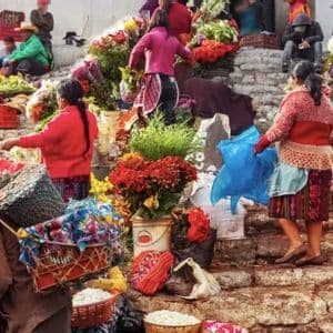 Un affollato mercato di fiori all'aperto su una scalinata di pietra, con persone in abiti tradizionali che acquistano e vendono bouquet colorati.