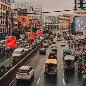 An elevated view of a busy city street with heavy traffic on a rainy day, surrounded by buildings and billboards.