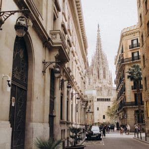 Una calle estrecha de la ciudad, flanqueada por edificios históricos de piedra, con la aguja de una catedral gótica visible a lo lejos.