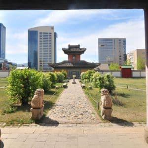 Un temple traditionnel dans une cour verdoyante est encadré par des piliers rouges, avec des gratte-ciel modernes s'élevant en arrière-plan.