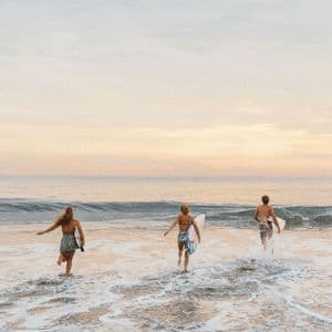 Un viaggio di gruppo WeRoad con tre surfisti che corrono nell'oceano con le loro tavole da surf all'alba.