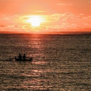 Silhouette di due persone in barca sull'oceano durante un vibrante tramonto arancione.