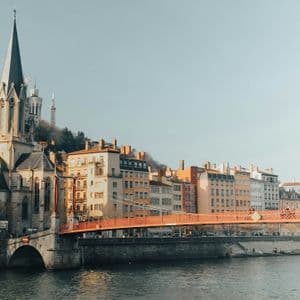 Un vivace ponte pedonale arancione attraversa un fiume di fronte a una città collinare con una grande chiesa ed edifici storici.