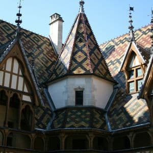 Un tetto in tegole smaltate di un edificio storico con motivi geometrici, visto da un cortile interno sotto un cielo azzurro.