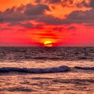 Le soleil se couche sur l'océan, projetant une lueur vibrante rouge et orange sur l'eau et un ciel nuageux.