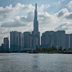Uno skyline moderno con un grattacielo imponente, visto da oltre uno specchio d'acqua sotto un cielo parzialmente nuvoloso.