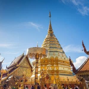 Un grand stupa doré et des bâtiments de temple ornés se dressent sous un soleil éclatant et un ciel bleu clair.