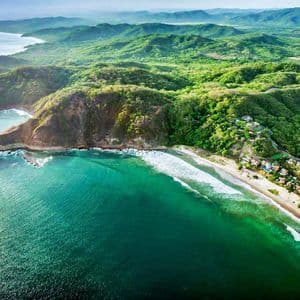Veduta aerea di una vibrante costa verde con acqua turchese che lambisce una spiaggia sabbiosa e scogliere.