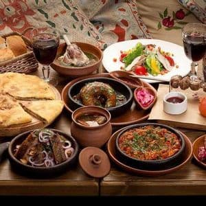 Eine reichhaltige Auswahl traditioneller Speisen, darunter Eintöpfe, Fladenbrot, Salate und gegrilltes Fleisch, serviert mit Rotwein auf einem Holztisch.