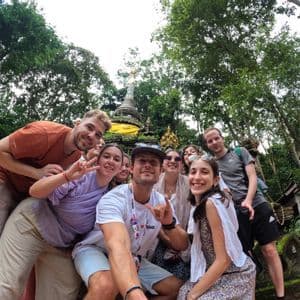 Un gruppo WeRoad in posa per un selfie davanti a uno stupa di pietra circondato da alberi rigogliosi.