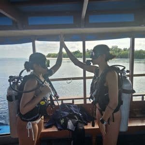 Dos mujeres de un viaje grupal de WeRoad con equipo de buceo se chocan las cinco en un barco en el océano.