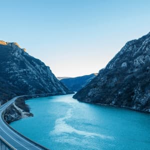 Vue aérienne d'un pont avec une route sinueuse longeant une rivière bleu vif traversant un canyon montagneux escarpé.