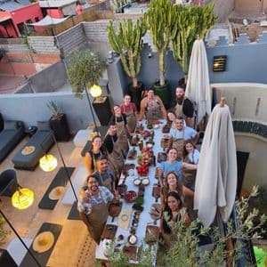 Un grupo de viaje de WeRoad con delantales, sonriendo alrededor de una mesa larga durante una clase de cocina en una terraza en la azotea.