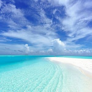 Un'unica persona su un banco di sabbia bianca, circondata da acque turchesi poco profonde e un vasto cielo azzurro con nuvole sparse.