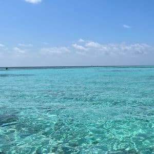 Acqua di mare limpida e turchese increspata sotto un cielo azzurro brillante con poche nuvole e una barca all'orizzonte.