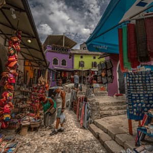 Les gens flânent devant les étals de souvenirs et de textiles d'un marché en plein air, dans une rue pavée étroite, entre des bâtiments colorés.