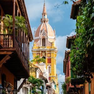 Un campanile colorato con una cupola rosa si erge alla fine di una strada fiancheggiata da edifici coloniali con balconi in legno.