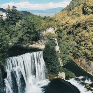 Une grande cascade se jette dans une rivière, entourée d'une forêt verdoyante, avec des maisons à flanc de colline en arrière-plan.