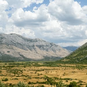 Un vaste paysage de vallée sèche, avec une montagne verdoyante d'un côté et une chaîne rocheuse de l'autre, sous un ciel bleu nuageux.