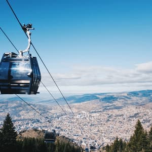 Un téléphérique moderne survole une ville tentaculaire dans une vallée montagneuse, avec des cimes d'arbres persistants en contrebas.