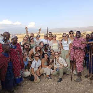 Un groupe WeRoad pose pour une photo avec des habitants vêtus de vêtements traditionnels dans un paysage ensoleillé et sec.
