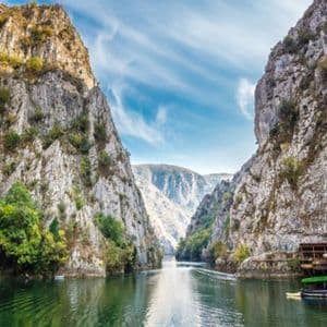 Ein Fluss fließt durch eine tiefe, felsige Schlucht mit bewaldeten Klippen unter einem blauen Himmel mit vereinzelten Wolken.