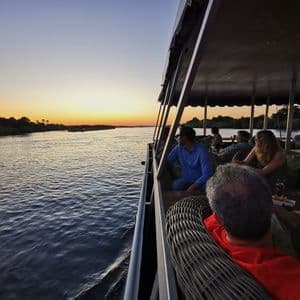 Un gruppo WeRoad in viaggio si rilassa sul ponte coperto di una barca ammirando il tramonto su un ampio fiume.