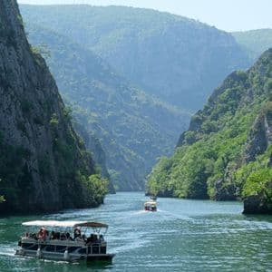 Eine WeRoad-Gruppenreise auf Ausflugsbooten, die an einem sonnigen Tag durch eine Flussschlucht mit steilen, bewaldeten Klippen gleitet.