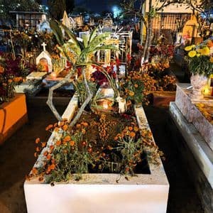 Ein Friedhof bei Nacht mit Gräbern, die mit zahlreichen orangefarbenen Ringelblumen und brennenden Kerzen geschmückt sind.