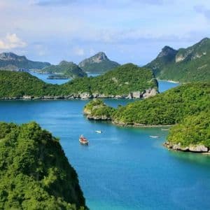 Une vue panoramique de nombreuses îles verdoyantes et luxuriantes, émergeant d'une mer bleue calme, avec quelques petits bateaux sur l'eau.