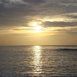 Le soleil se couche sur l'océan, son reflet doré scintille sur l'eau sous un ciel nuageux.