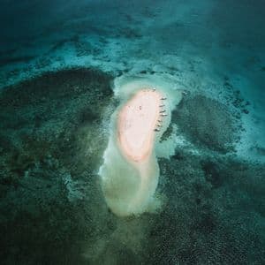 Una vista aerea di un viaggio di gruppo WeRoad su un remoto banco di sabbia rosa in un mare turchese, con diverse barche allineate sulla riva.
