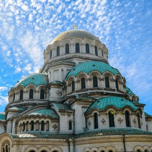 Una grande cattedrale con un'ampia cupola dorata e cupole turchesi più piccole contro un cielo azzurro brillante con nuvole bianche.