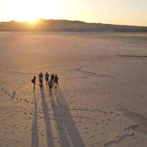 Veduta aerea di un viaggio di gruppo WeRoad in un vasto deserto al tramonto, che proietta lunghe ombre sul terreno arido e screpolato.