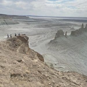 Un gruppo WeRoad di quattro persone in piedi sul bordo di una scogliera rocciosa, affacciato su un vasto canyon arido con guglie di roccia sotto un cielo nuvoloso.