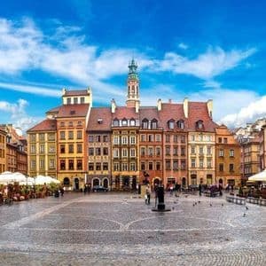 A wide cobblestone town square surrounded by colorful historic buildings and outdoor cafes under a bright blue sky.