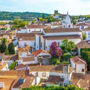 Eine Vogelperspektive einer historischen Stadt mit weiß getünchten Gebäuden, Terrakotta-Ziegeldächern und einer entfernten Burg auf einem grünen Hügel.
