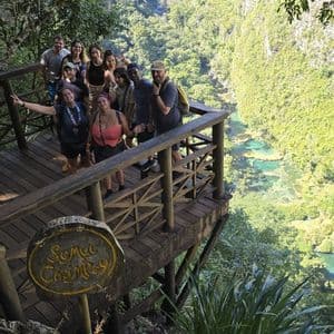 Un groupe WeRoad en photo sur un point de vue en bois, surplombant une vallée verdoyante et une rivière turquoise.