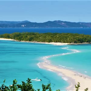 Un banc de sable blanc et sinueux s'étire d'une petite île arborée vers des eaux turquoise éclatantes, avec un bateau ancré à proximité.