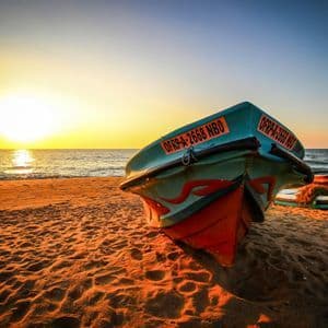 Un bateau de pêche coloré repose sur une plage de sable, le soleil se couchant sur l'océan, projetant une lueur dorée.